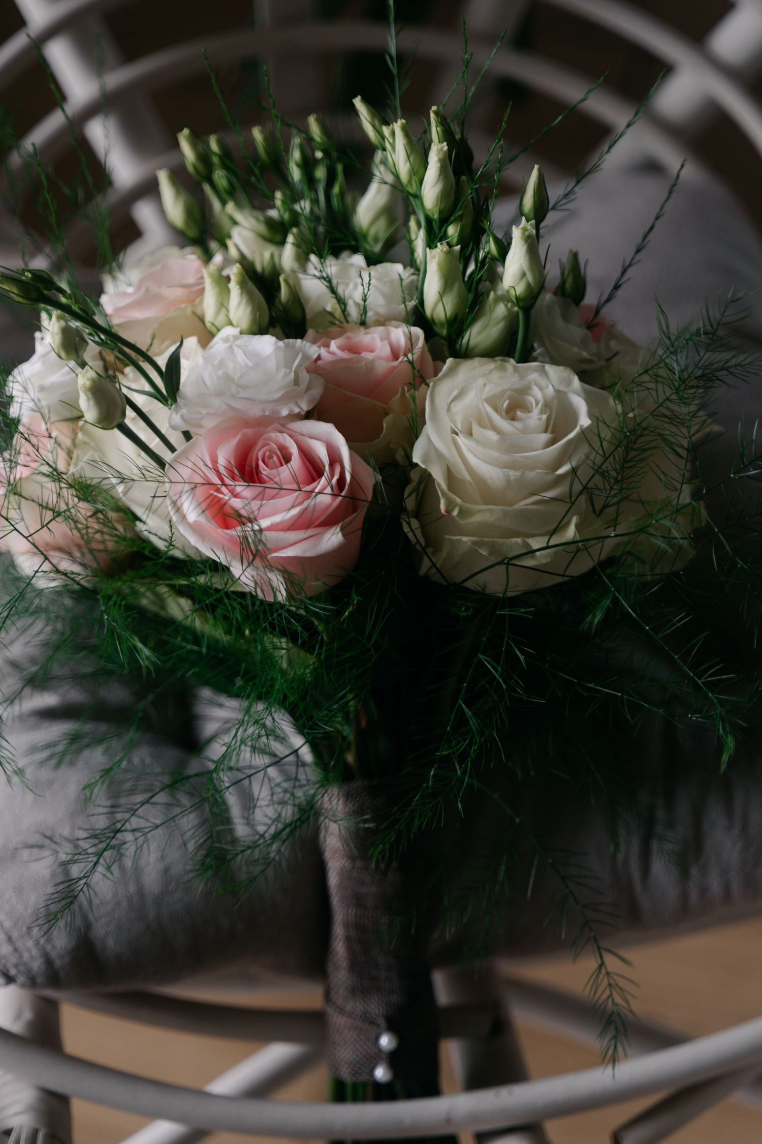 A romantic bouquet of pink and white roses with delicate greenery in a dark vase against a blurred background.