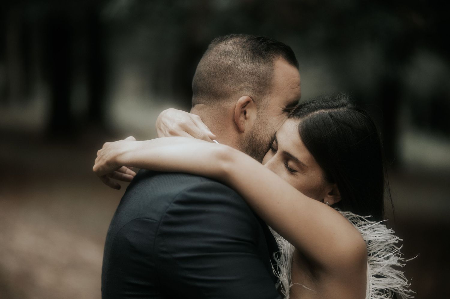 A romantic couple embraces in an intimate moment outdoors with a soft, dreamy forest backdrop.