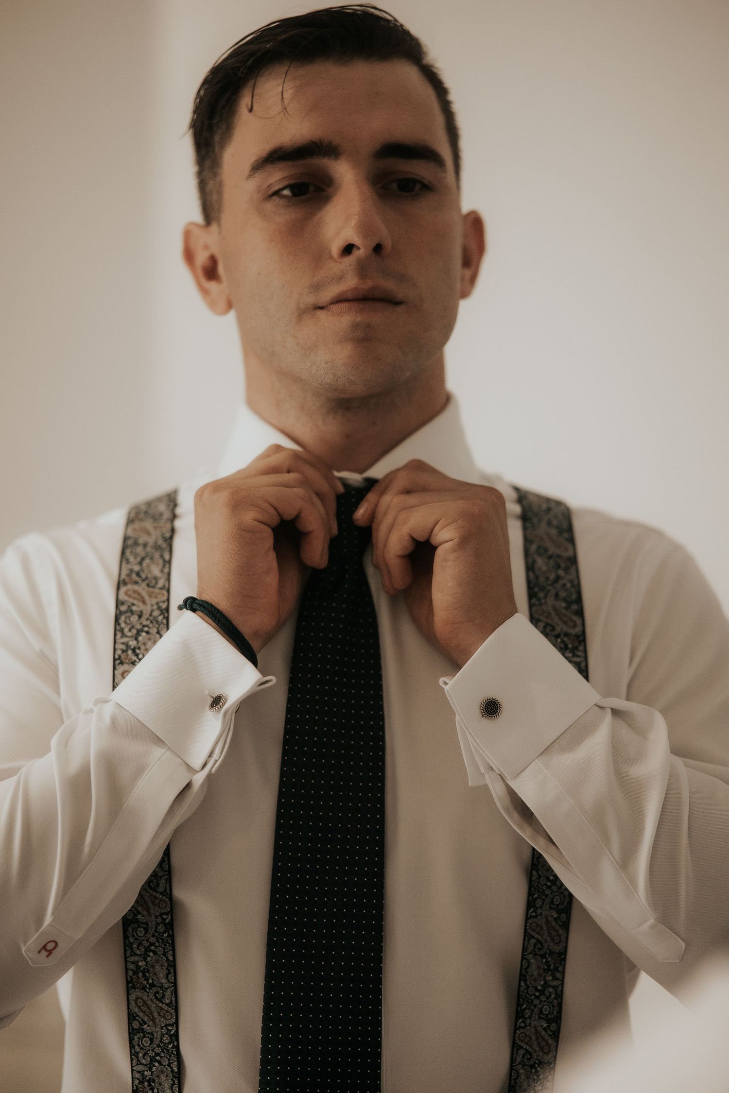 A series of four photos showing someone adjusting a polka dot tie while wearing a white dress shirt and patterned suspenders.