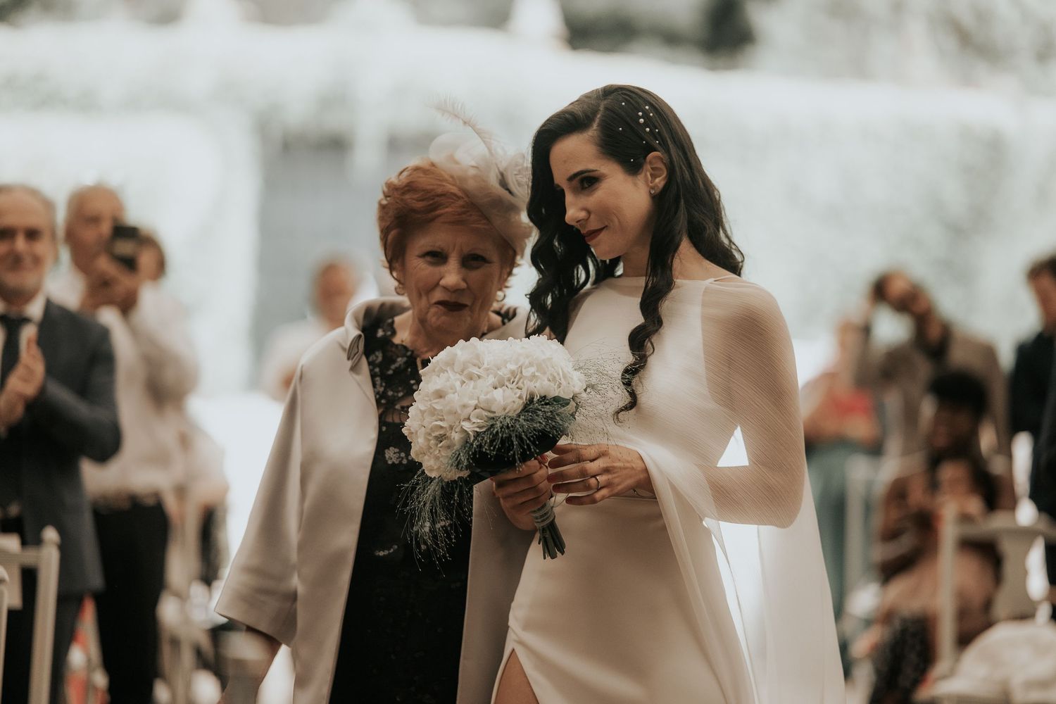 A tender moment at an outdoor wedding ceremony with guests looking on as a white bouquet is held.
