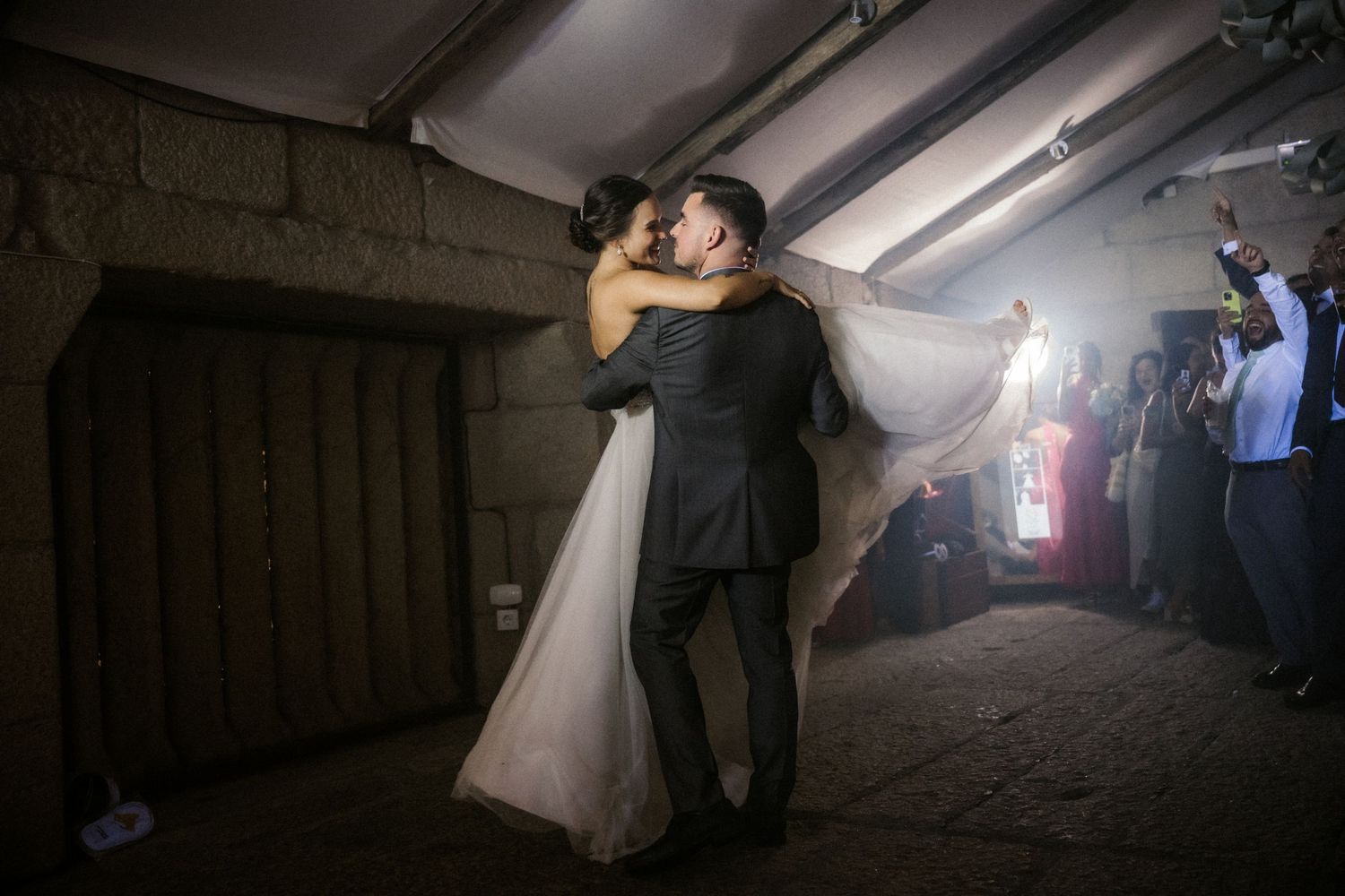 Newlyweds share an intimate dance moment in a dimly lit venue with atmospheric fog and backlighting.