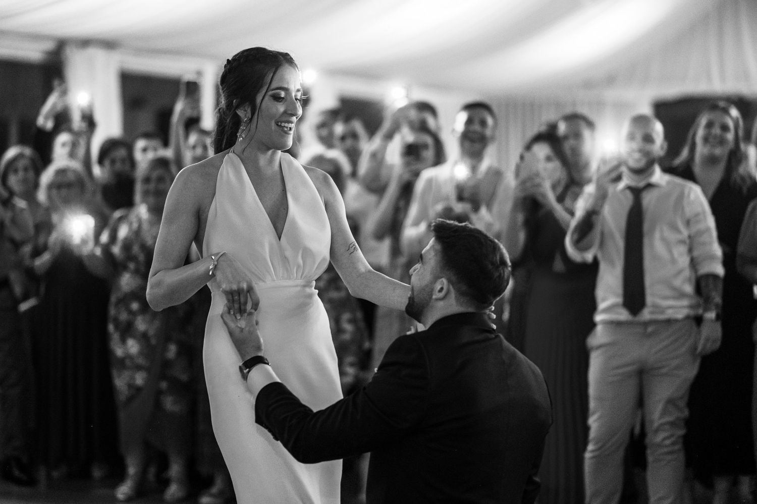 A tender moment during a wedding first dance as guests watch from the background in a tented reception venue.