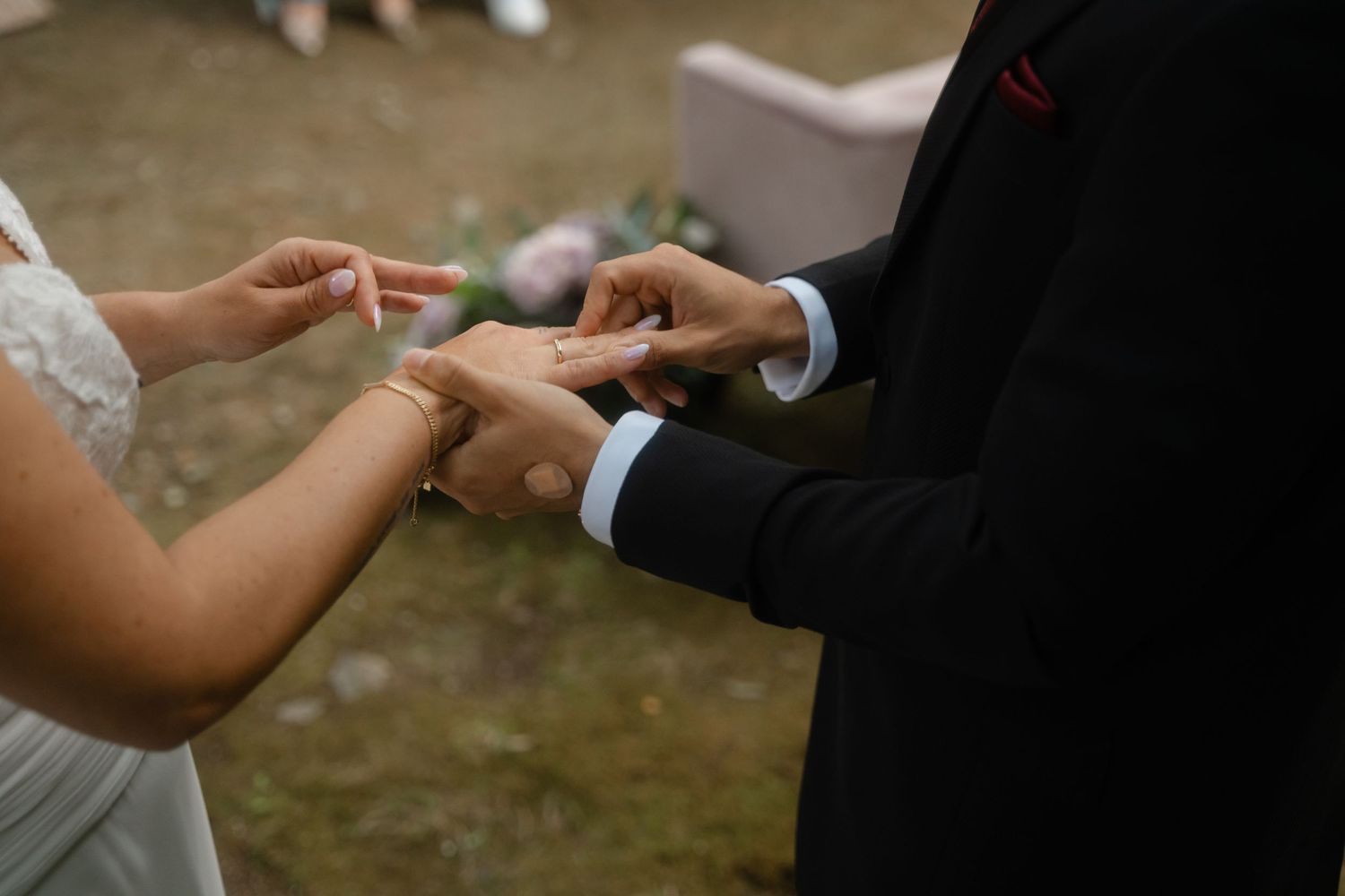Close-up of hands exchanging rings during an outdoor wedding ceremony.