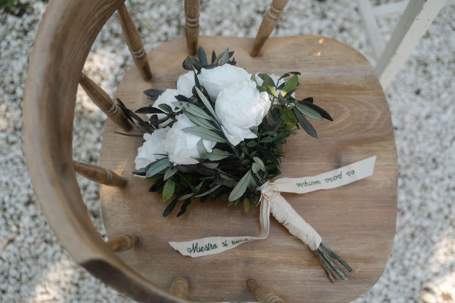 White floral boutonnieres with delicate greenery rest on a rustic wooden surface in a wedding setting.