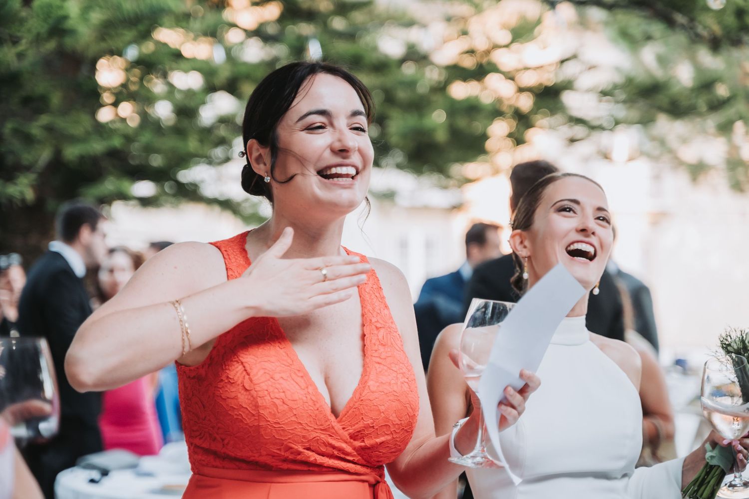 Wedding guests in bright coral dresses enjoying a festive outdoor reception celebration.