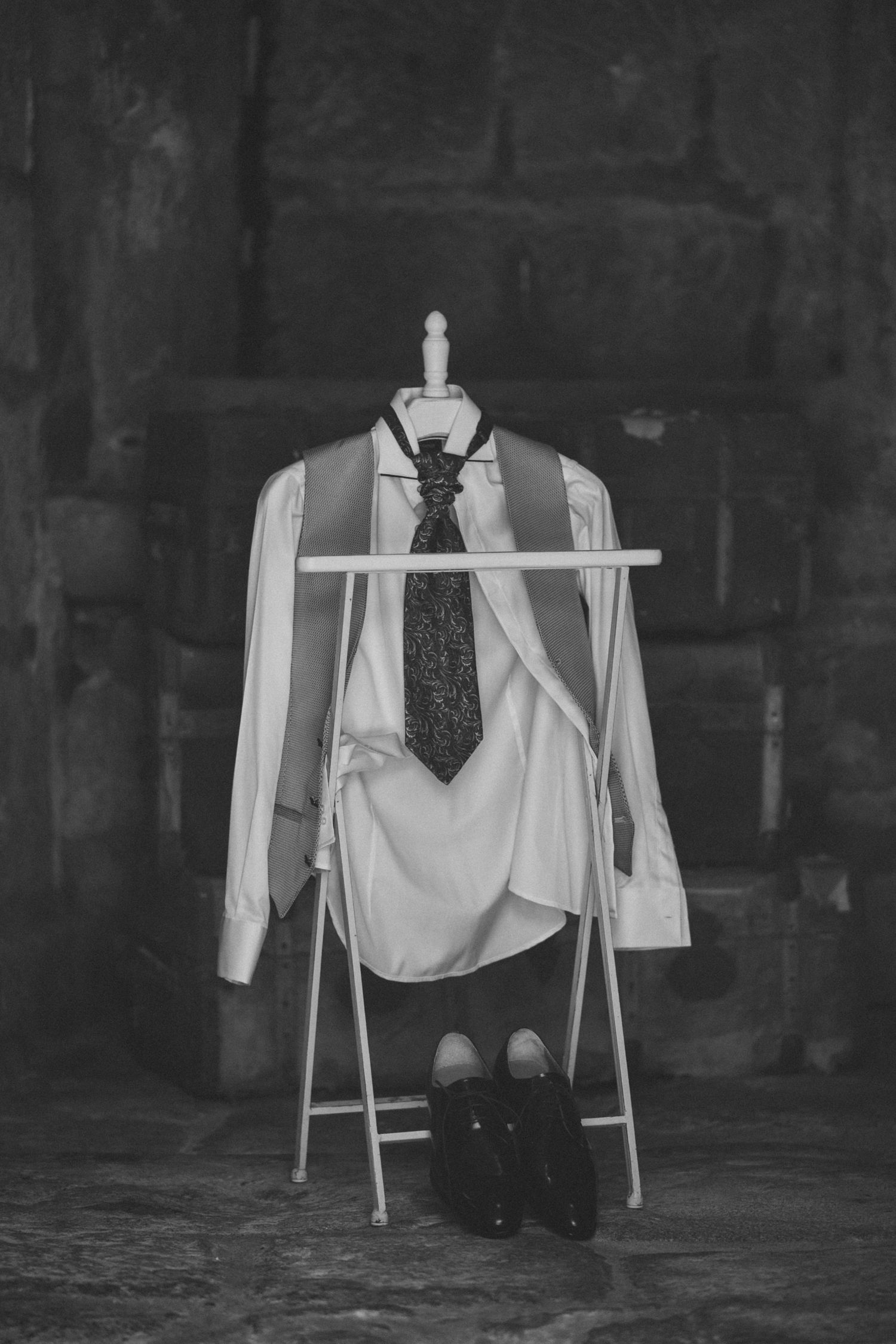 Black and white photo of formal attire including dress shirt and tie displayed on white clothing rack.