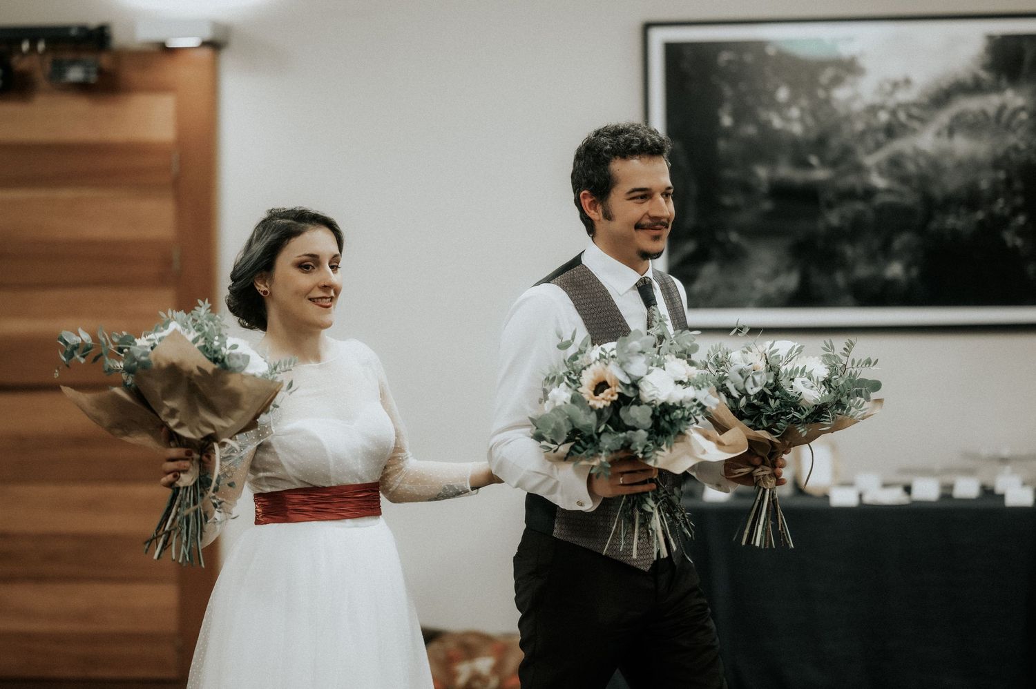 A wedding celebration with couples holding bouquets of flowers in an indoor venue with wooden walls.