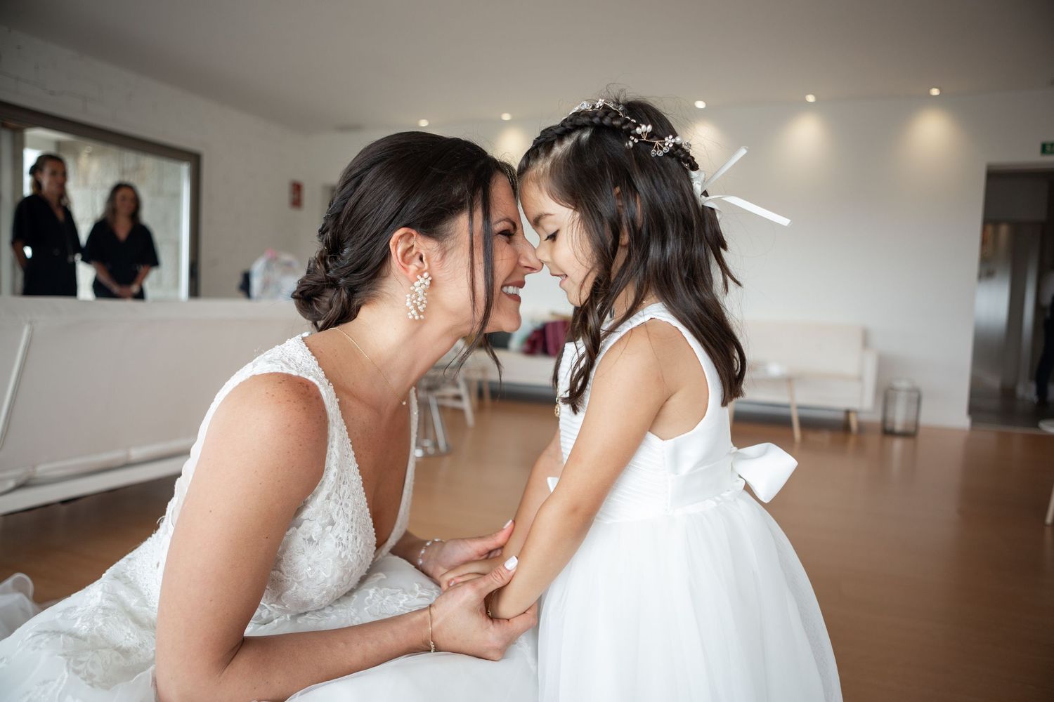 An intimate moment between a bride in a white dress and a young flower girl in a matching white dress.