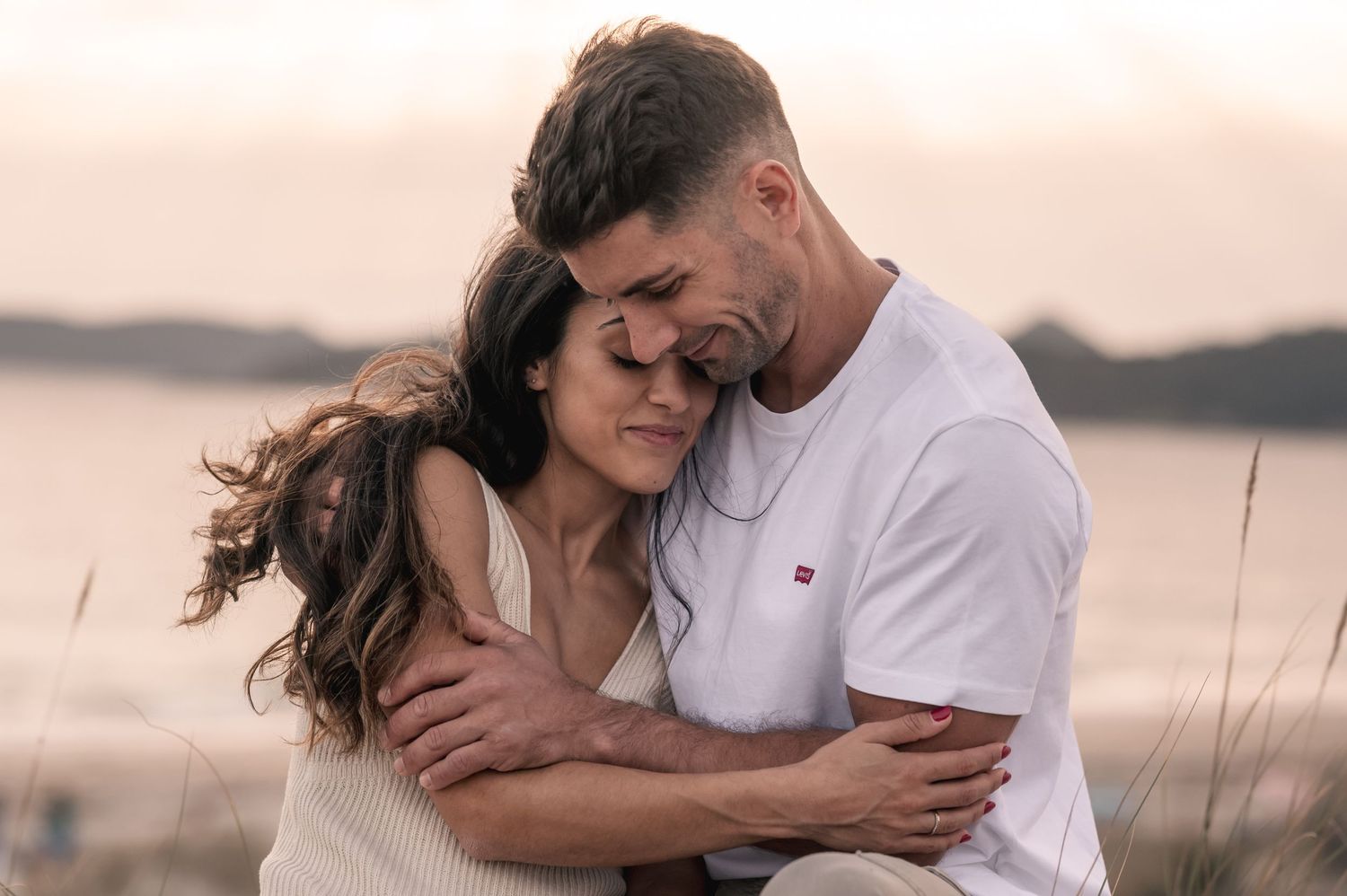 Romantic couple embracing tenderly at sunset by a serene lake with warm lighting and gentle breeze.