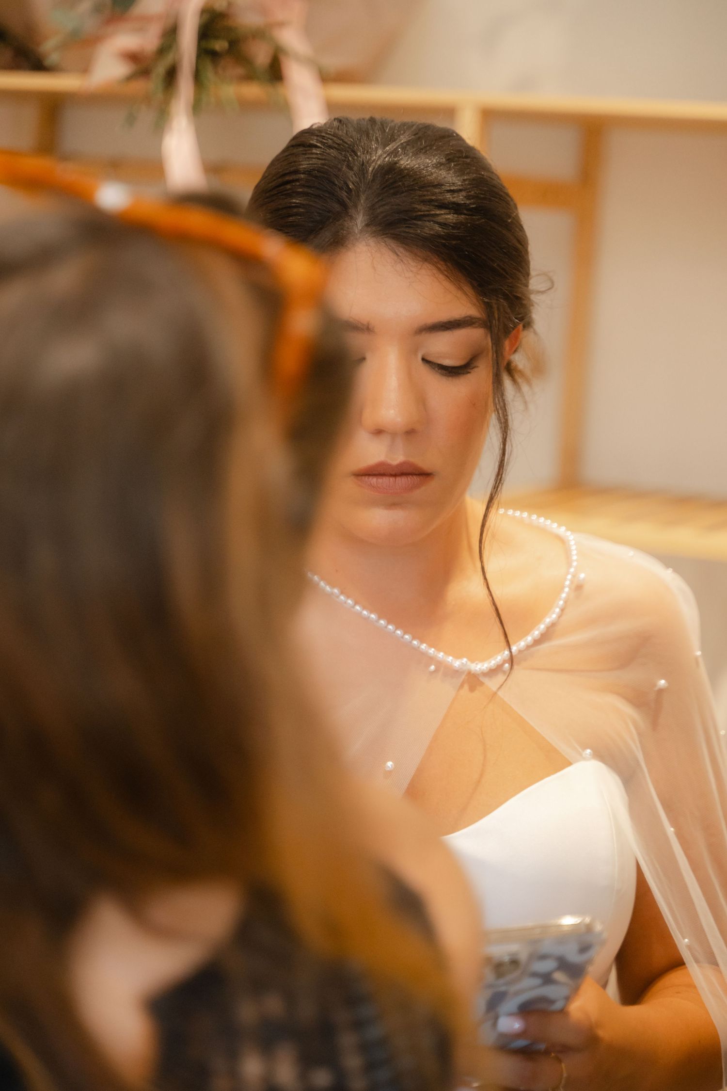 Soft focus portrait in warm lighting showing delicate pearl necklace and bridal details.
