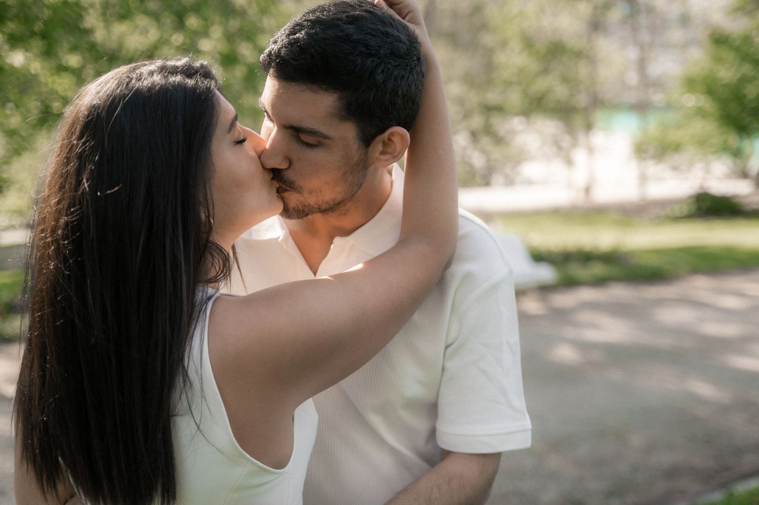 A romantic couple in white outfits shares intimate moments in a sunlit outdoor setting.