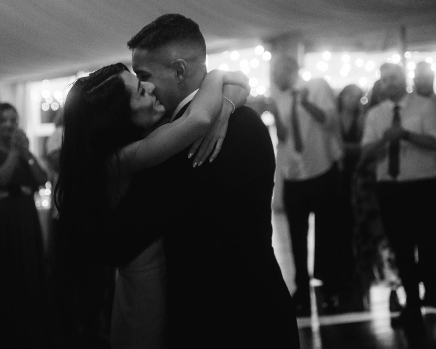 Wedding guests dancing and embracing on a dimly lit dance floor during an evening reception celebration.