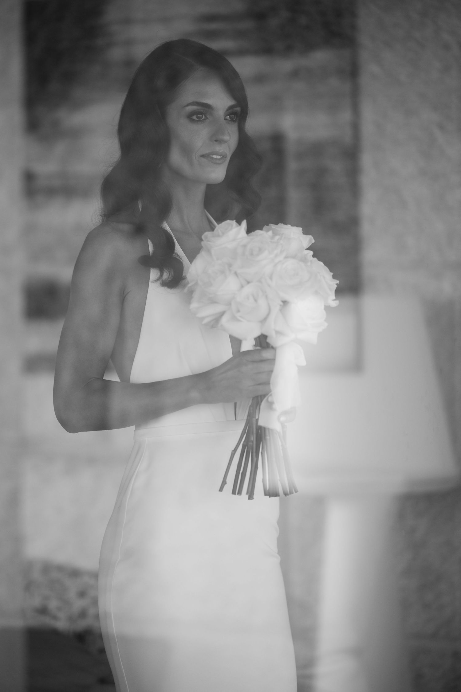 Bride in a one-shoulder white gown holds a classic white bouquet in a series of soft-focus portraits.