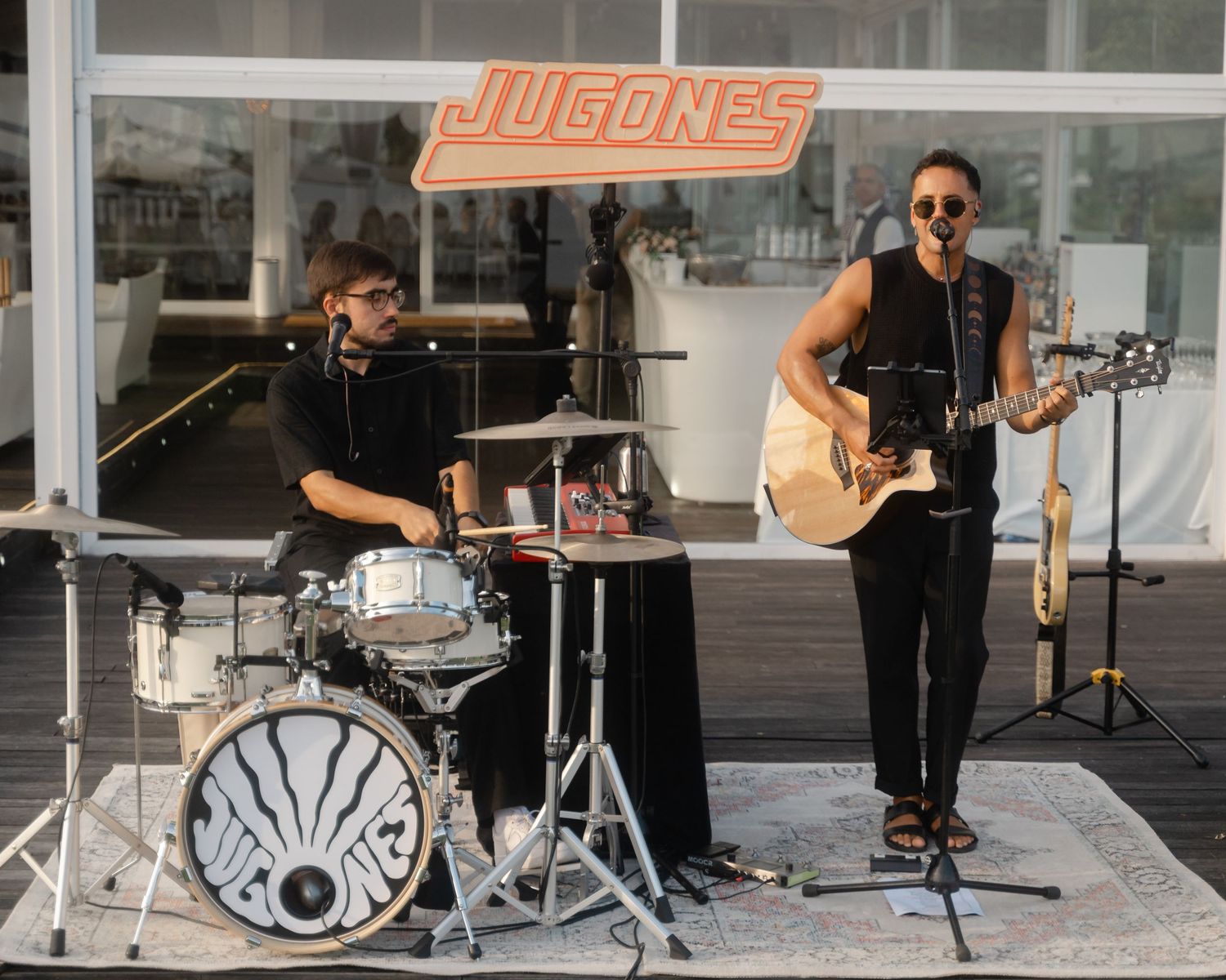 Live band performs on stage with instruments including drums, guitar and microphone setup.