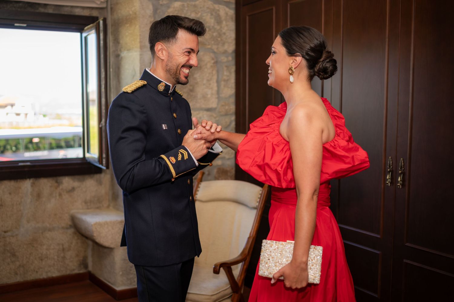 Two people share a joyful moment as they interact while dressed in formal attire - a military uniform and red gown.