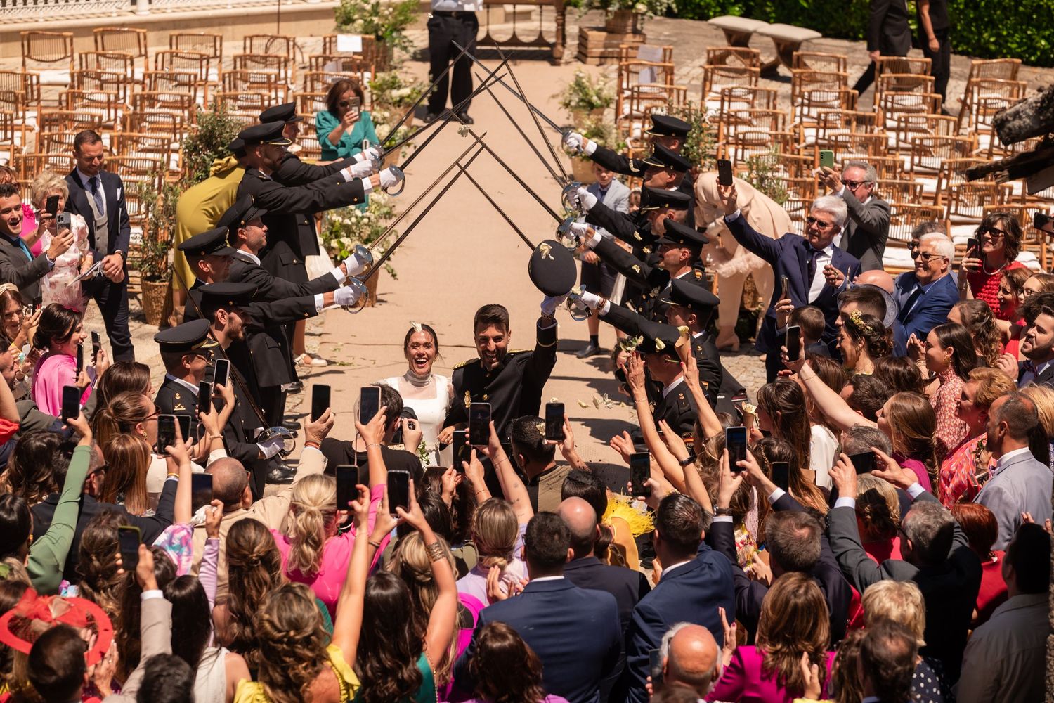 Large crowd of wedding guests celebrates outdoors in front of a historic stone building facade.