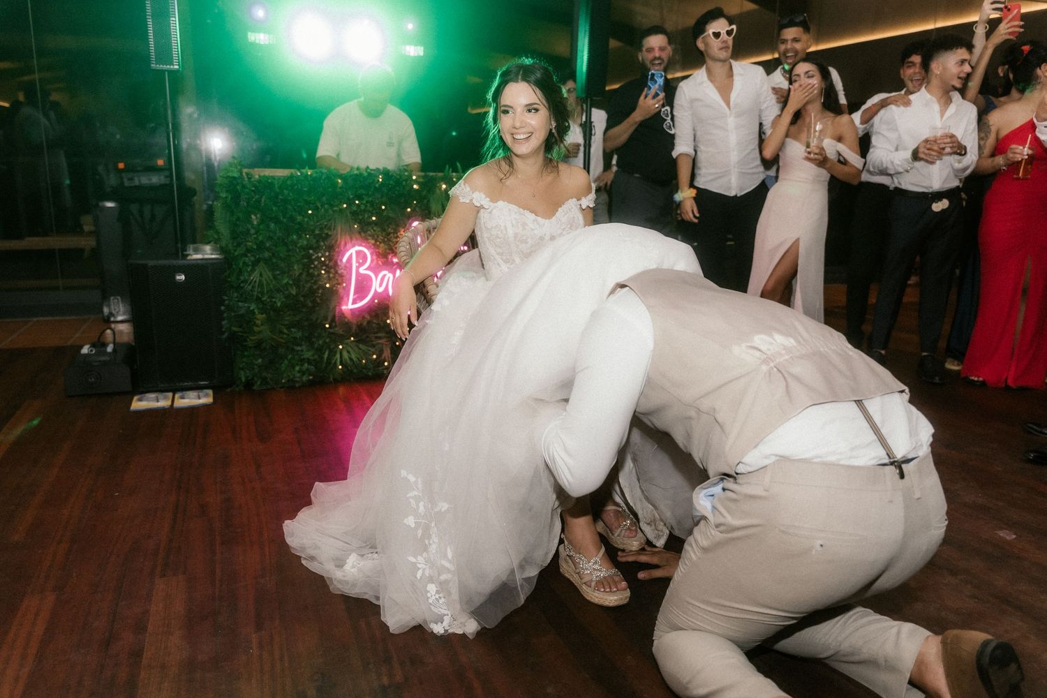 Wedding party dancing and celebrating on dance floor with green lighting at reception venue.