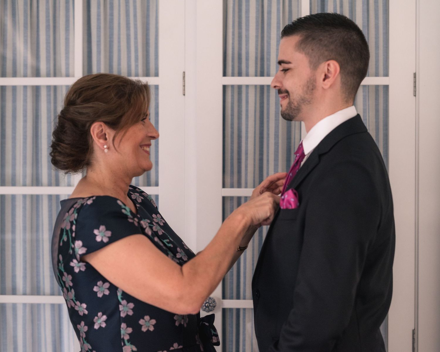 A couple in formal attire share a playful dance moment in front of white curtains.