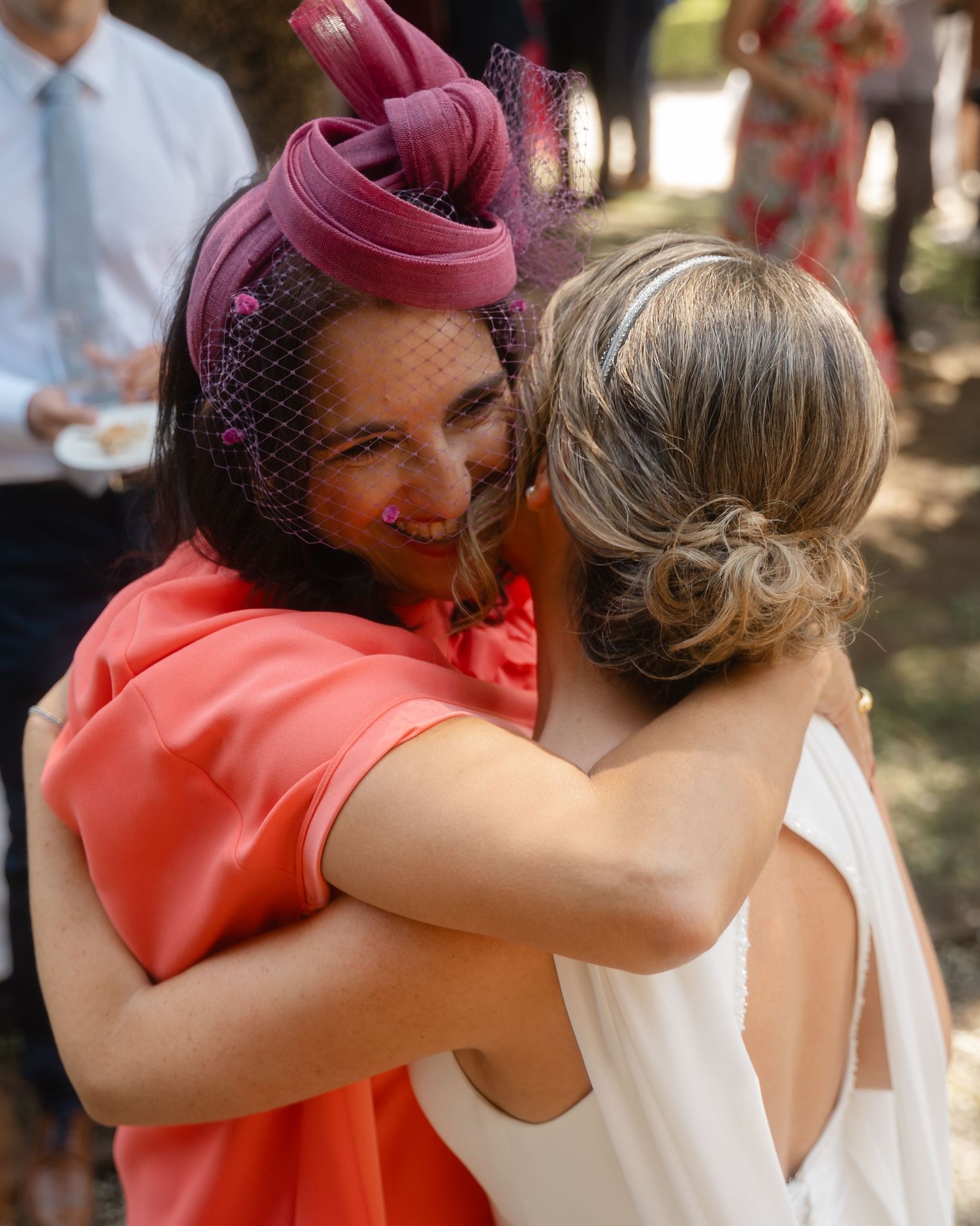 Wedding guests share emotional hugs and embraces while wearing bright coral colored attire.