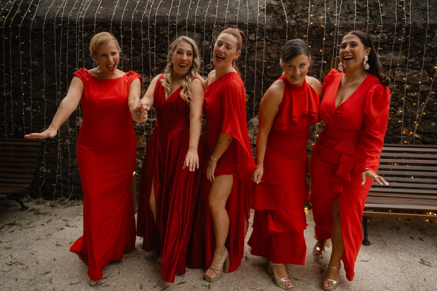 Group of bridesmaids in matching red dresses posing together outdoors at a wedding celebration.