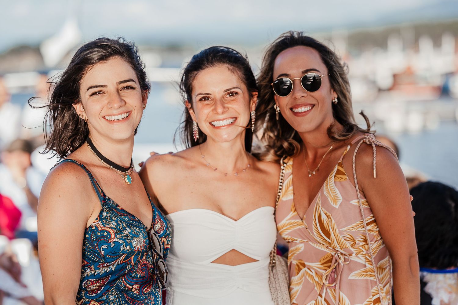 A group of people smile together at an outdoor waterfront gathering.