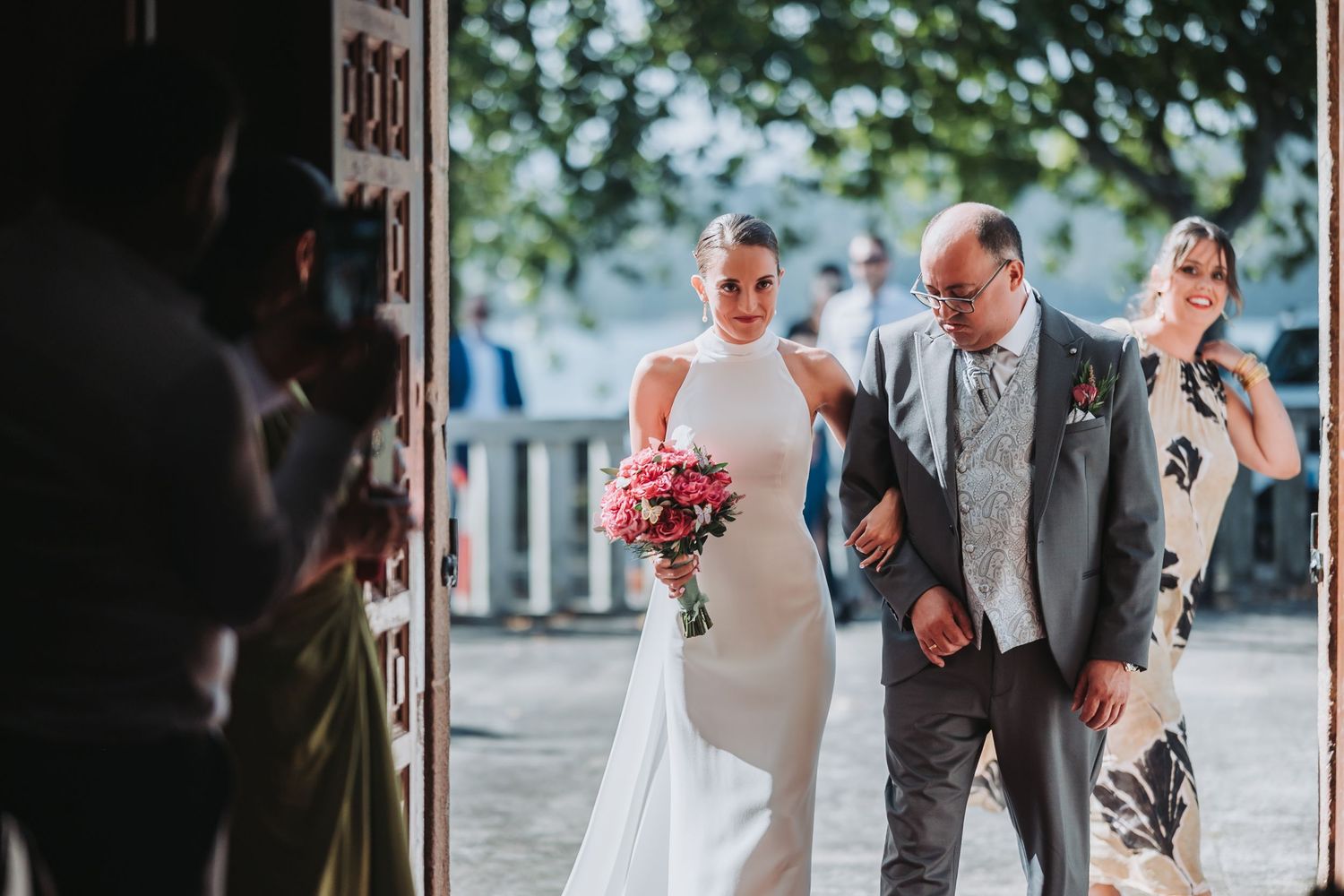 Wedding party gathers in a beautiful outdoor courtyard with stone archways and lush greenery.