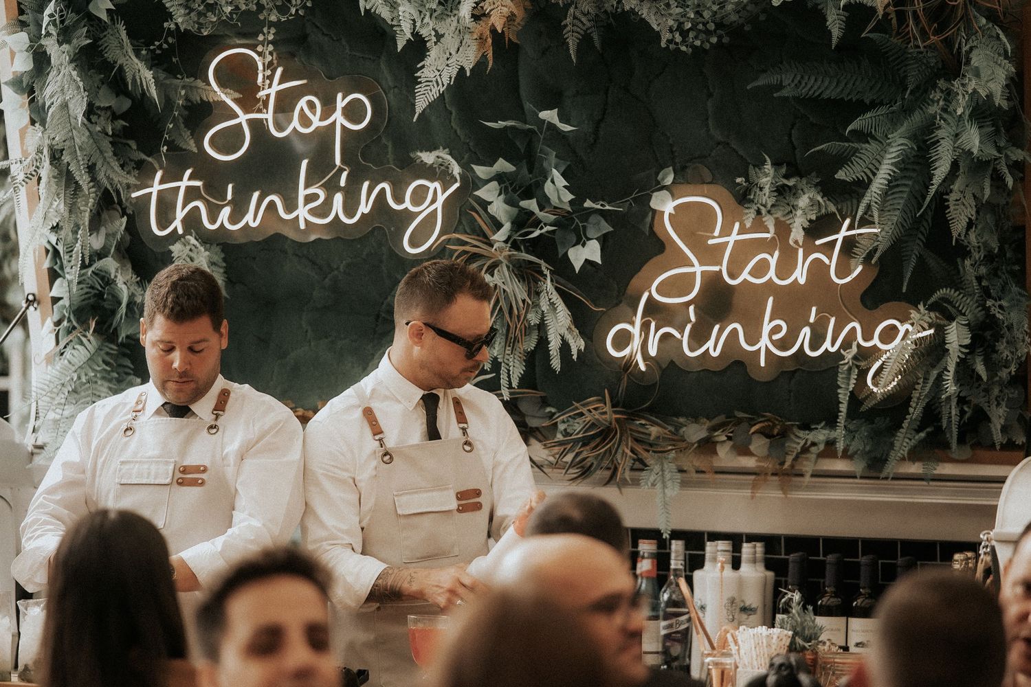 Neon signs displaying wedding-related text illuminate a rustic outdoor celebration space.