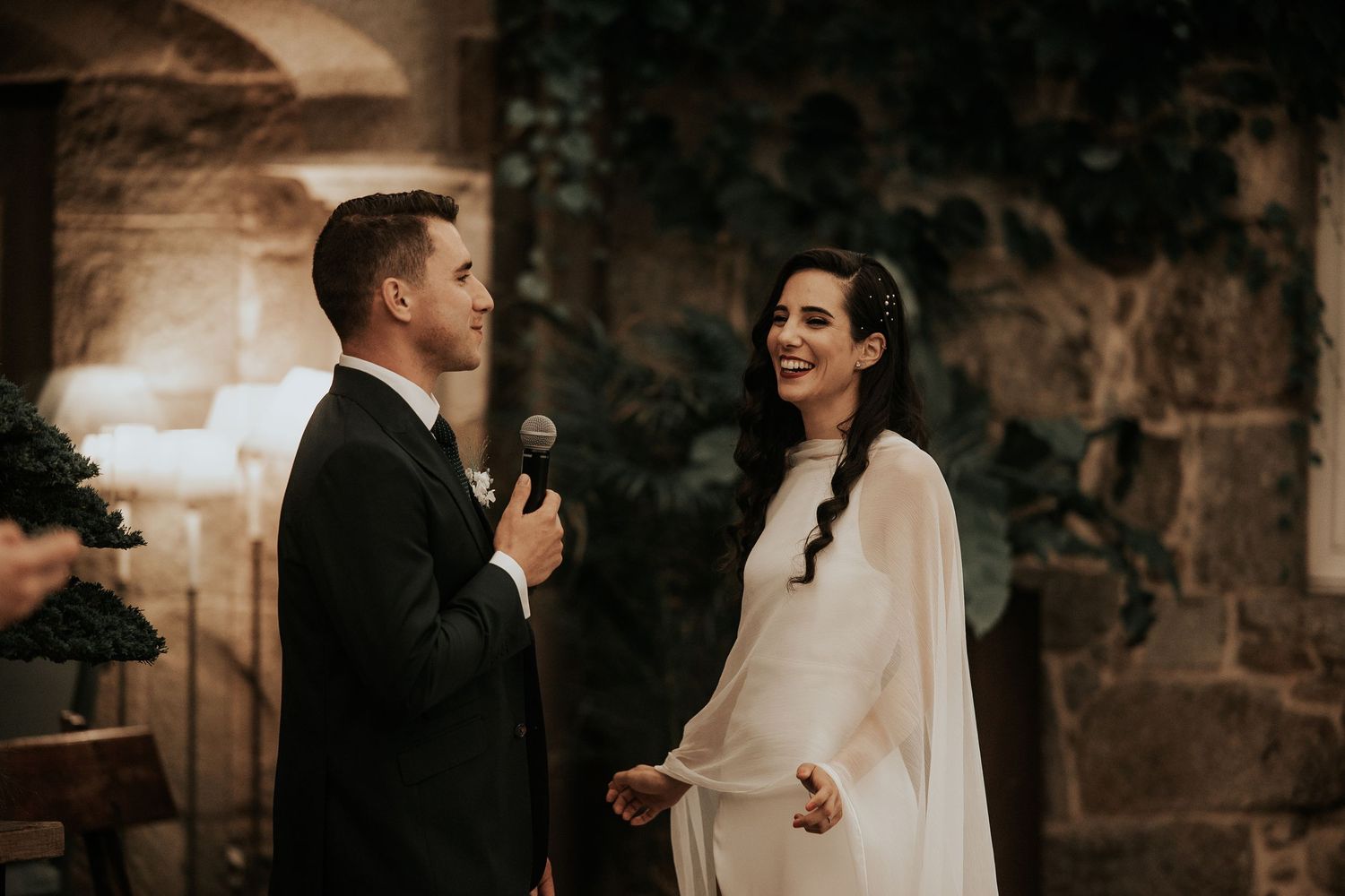 A romantic couple in formal wedding attire shares intimate moments in a dimly lit stone archway setting.