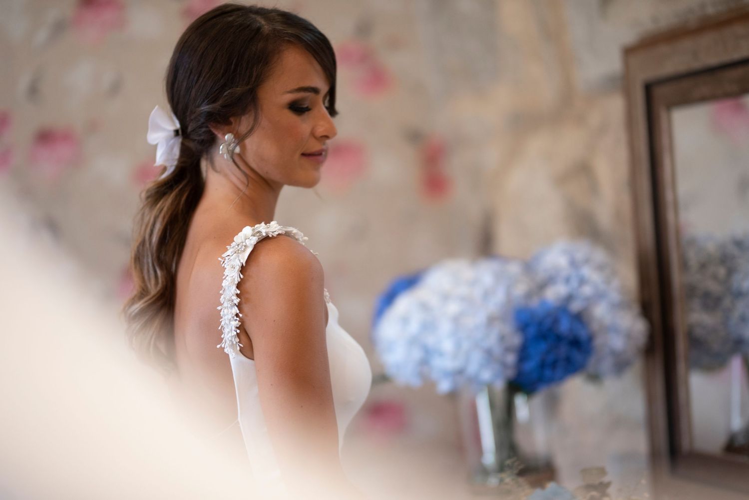 Elegant bride in white dress with dark hair and makeup getting ready for wedding ceremony.