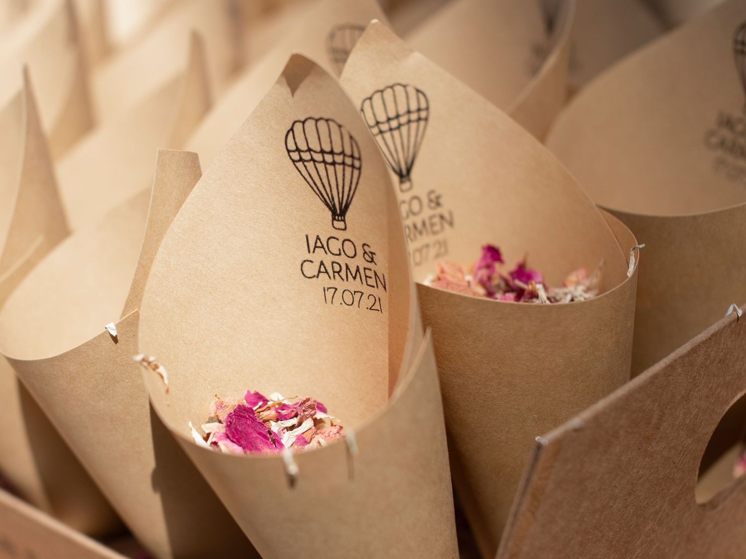 Small paper cones filled with pink flower petals arranged in a row for wedding confetti or decoration.