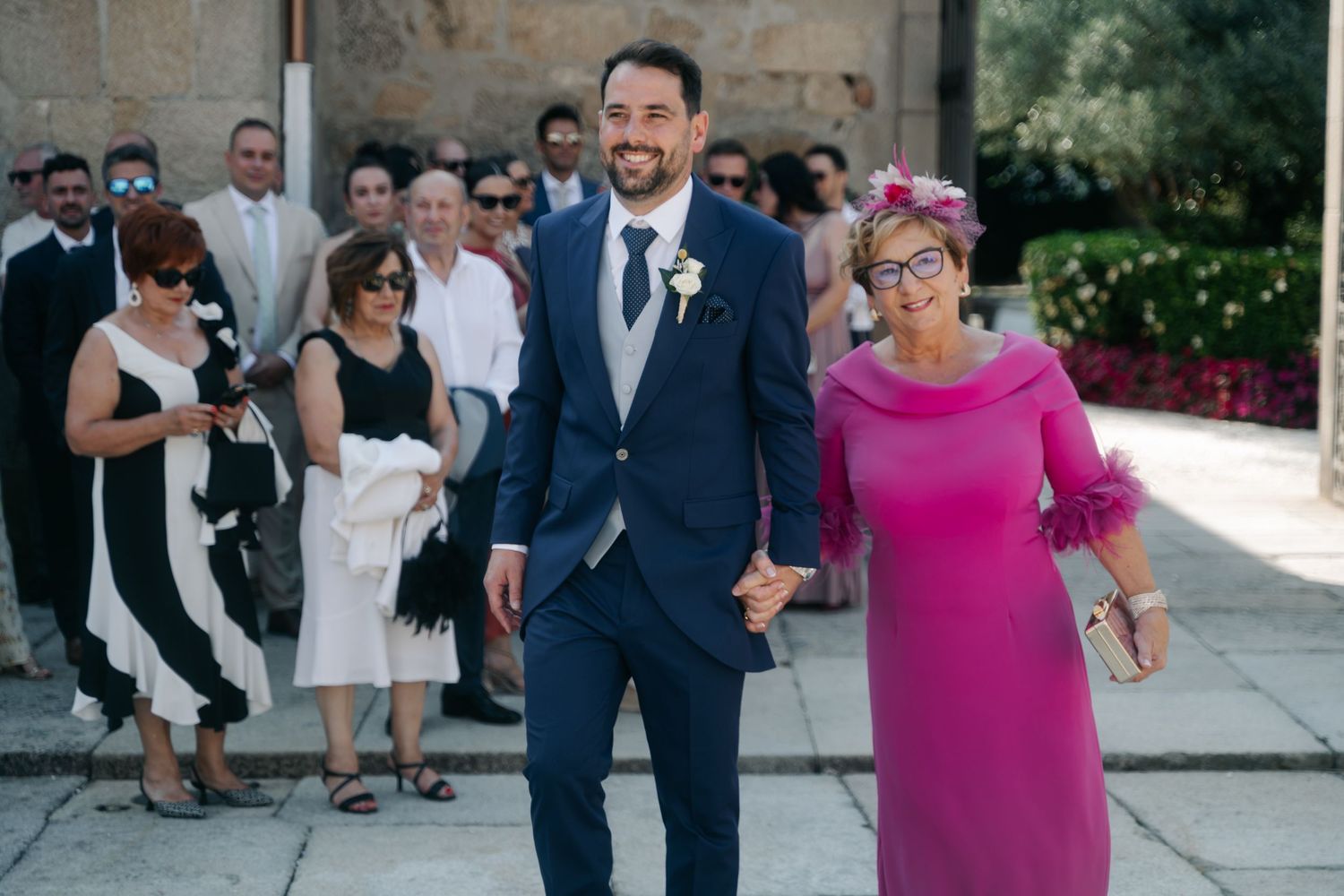 Wedding guests gathered outdoors at a stone venue during a sunny celebration.