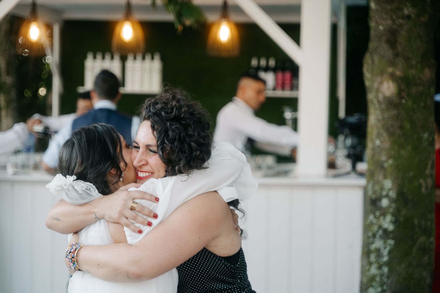 A couple embraces during their wedding celebration under warm string lights at an outdoor evening venue.