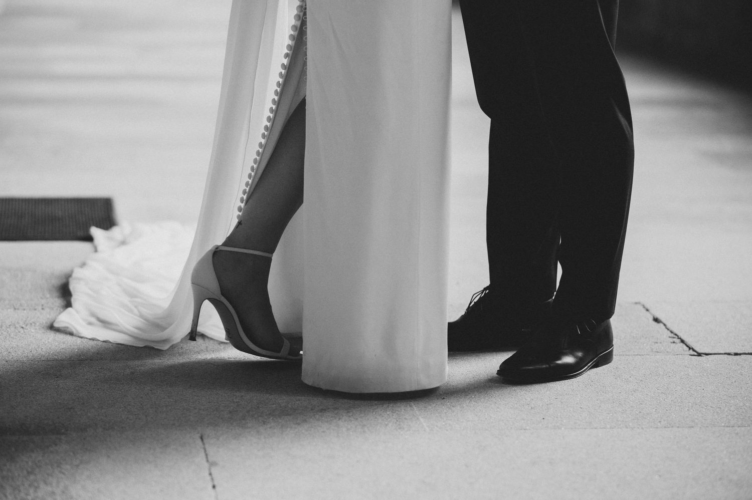 Black and white photograph showing elegant wedding dress details and formal shoes.