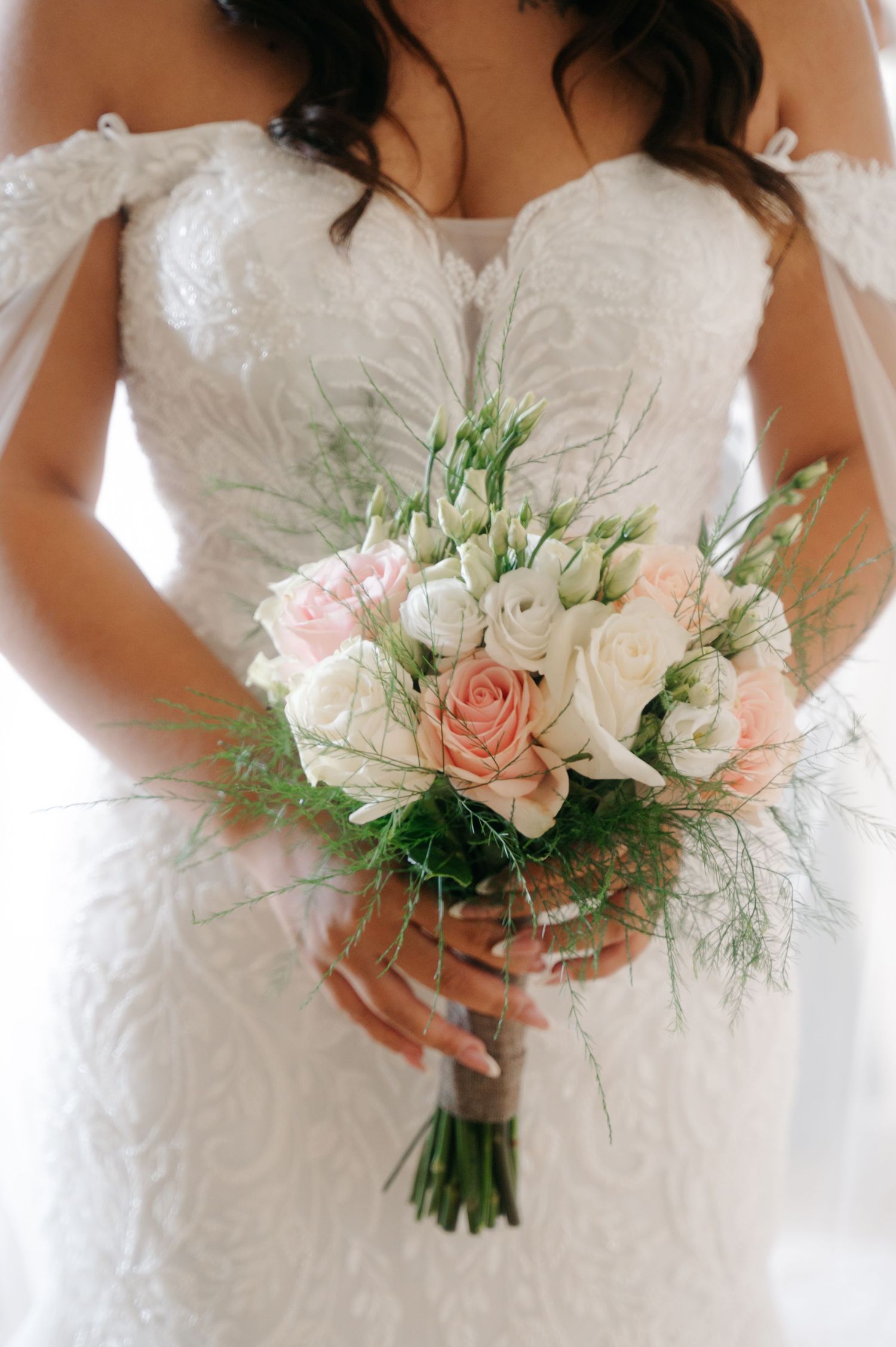 Four elegant white wedding bouquets with blush pink roses and delicate greenery held by bridesmaids in white dresses.
