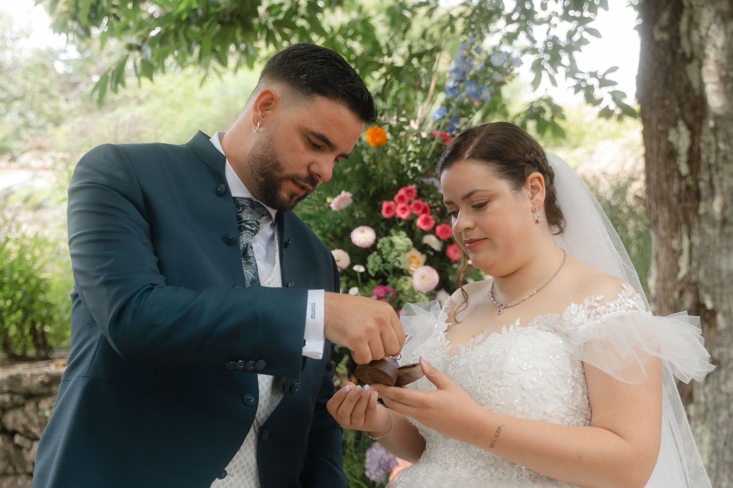 A couple in wedding attire shares a sweet moment together outdoors beneath trees on their special day.