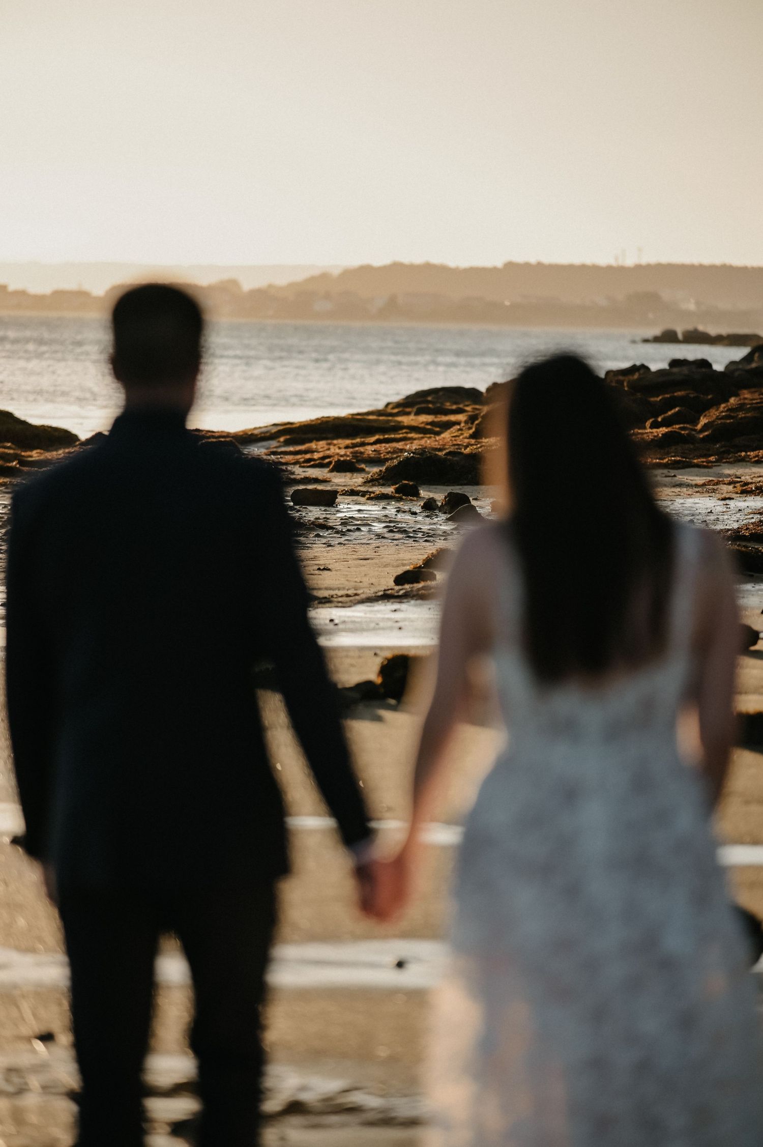 Silhouetted figures stand together on a rocky beach at sunset.