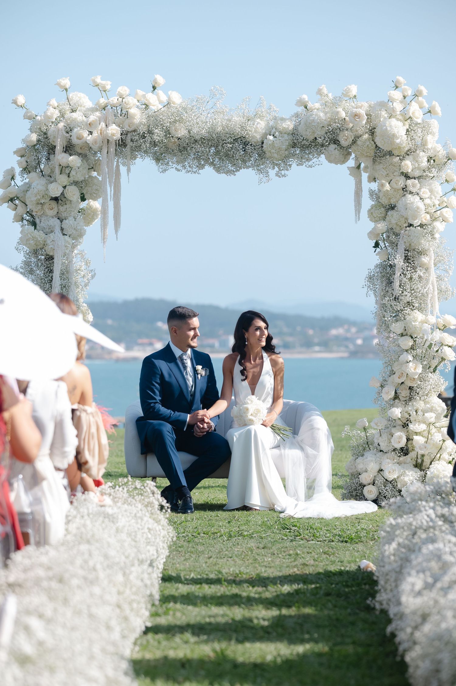 Beautiful outdoor wedding ceremony setup with white floral arches overlooking a waterfront view.