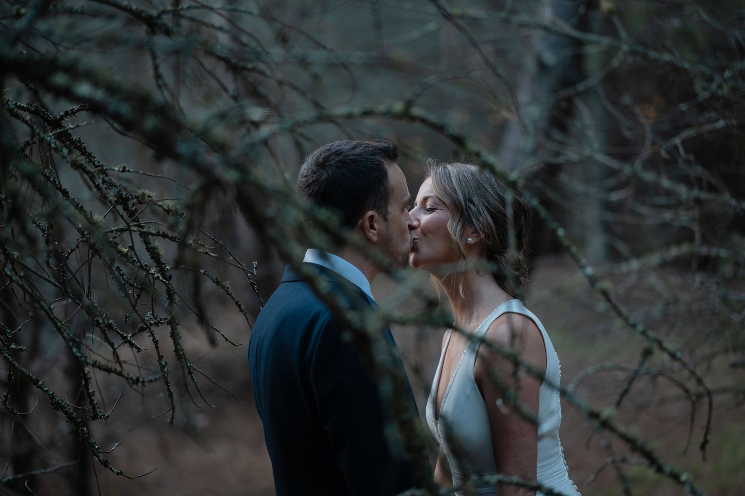 A romantic couple shares a tender moment in a moody forest setting during their wedding photoshoot.