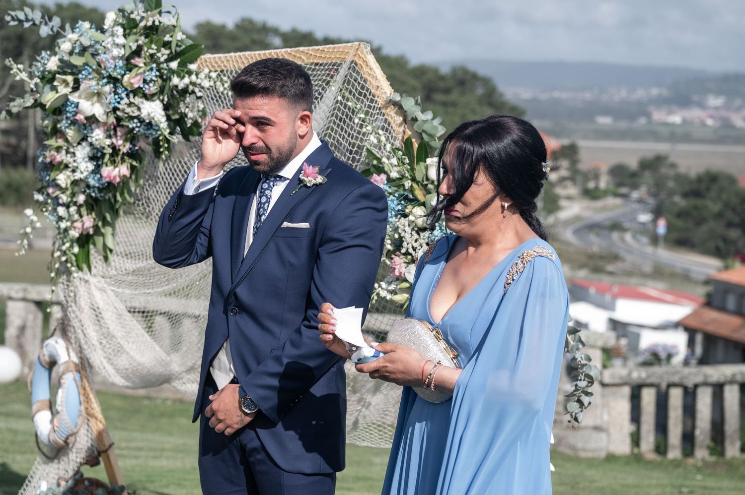 Couple enjoying drinks outdoors under floral arch during elegant outdoor celebration.