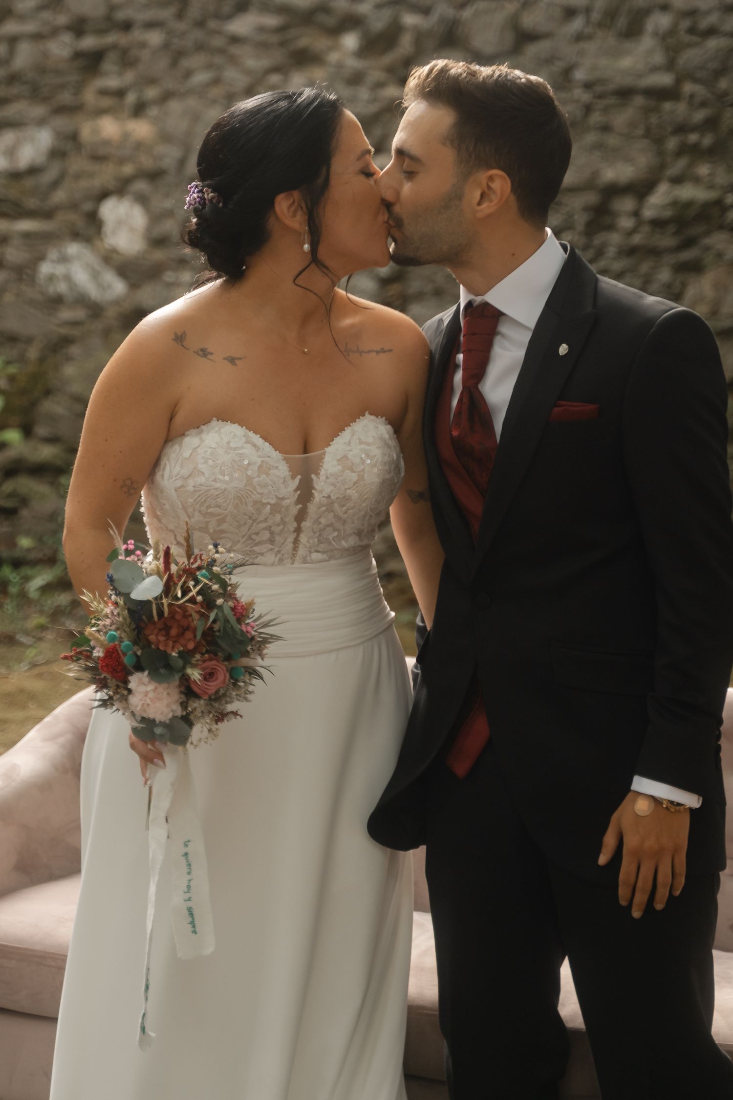 Newlywed couple shares intimate moments in a series of romantic poses against a stone wall backdrop.