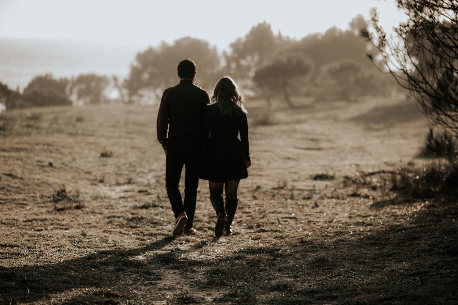 Silhouetted couple walking together on a scenic hilltop path at sunset.