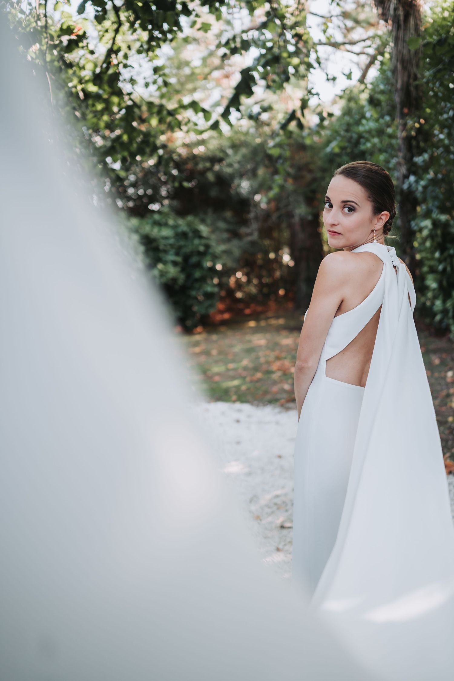Elegant bride in white dress with flowing veil poses in a garden setting.