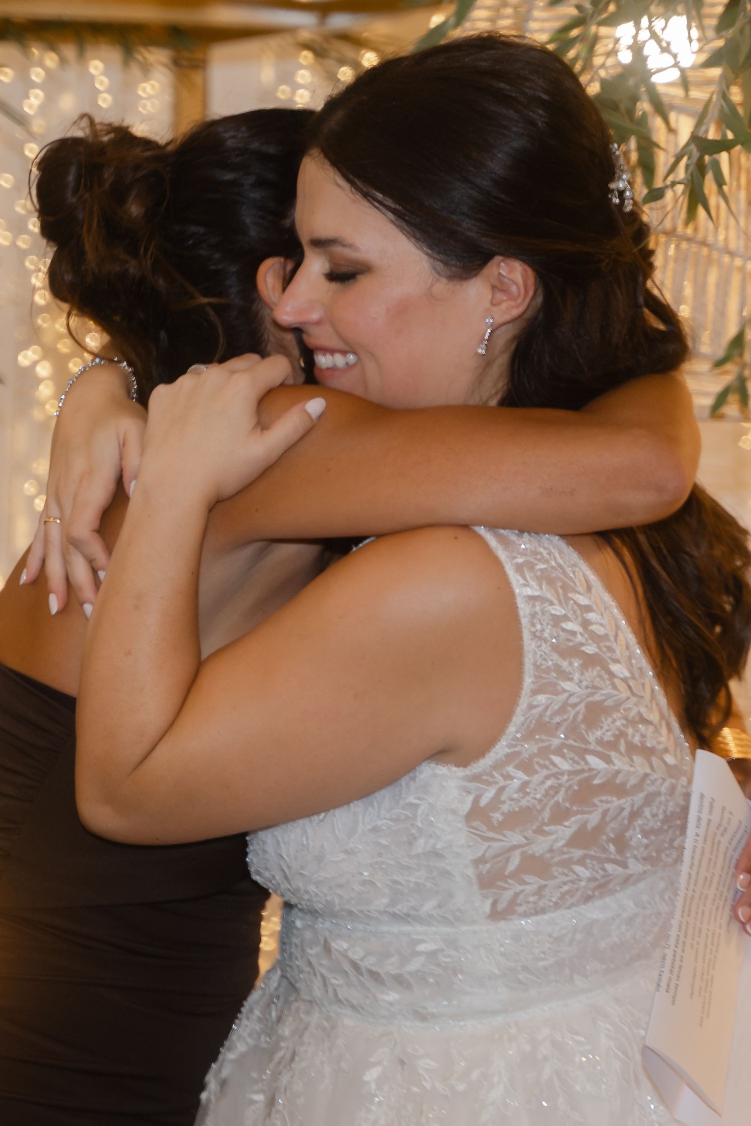 Two people share an emotional embrace in white lace and black formal attire at a special event.