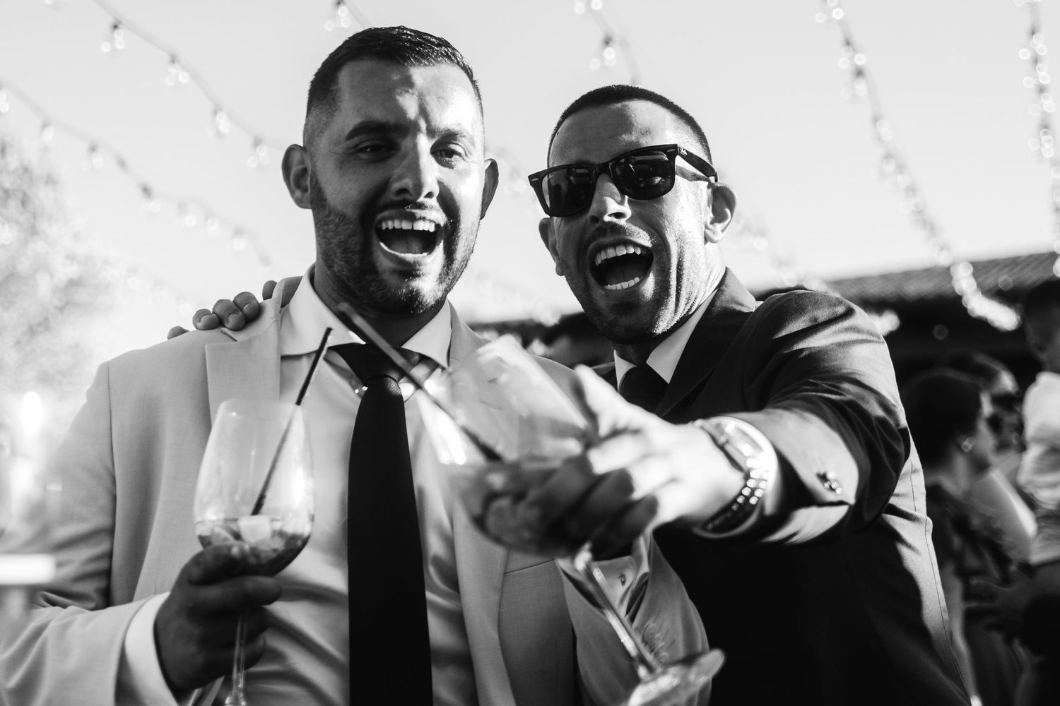 Two friends in formal attire share a candid laughing moment at an outdoor event.