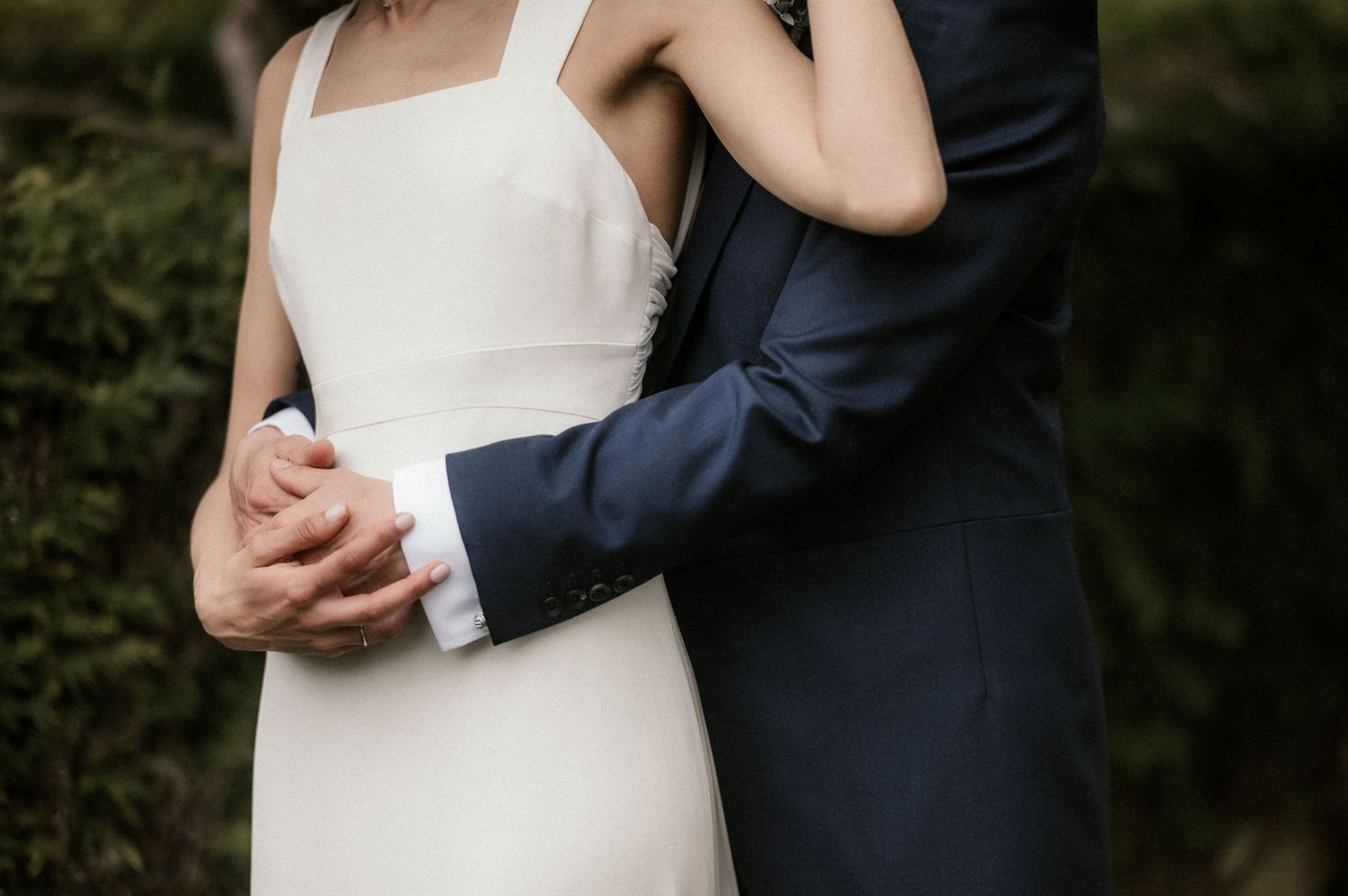 A romantic close-up of a couple embracing in wedding attire against a dark background.