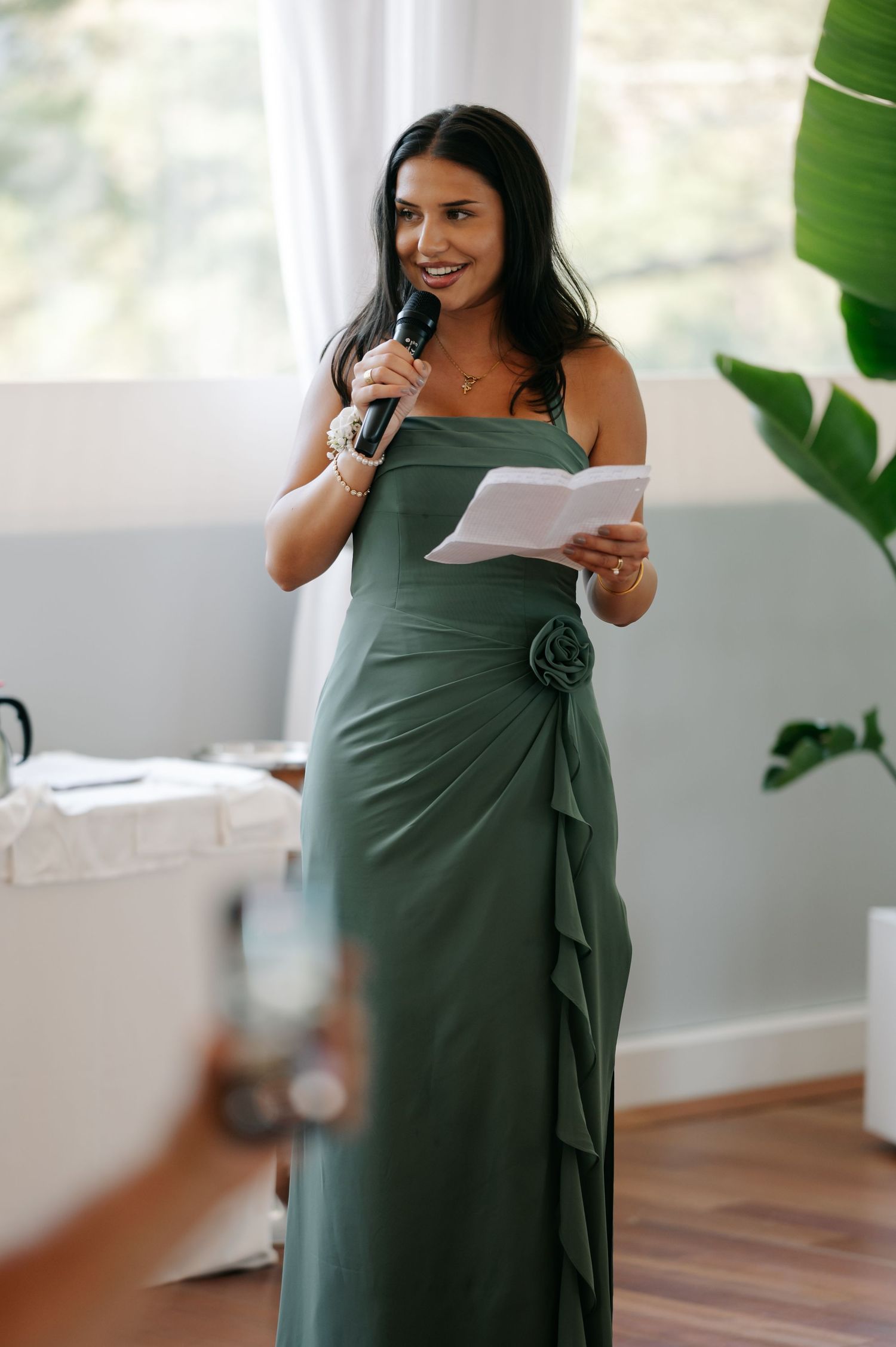Woman in a sage green wrap dress reacting emotionally while reading a letter in a bright room.