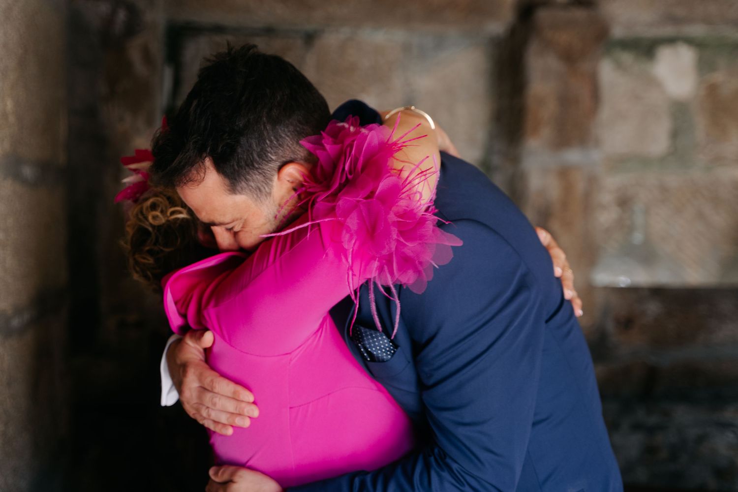 A couple dancing together in a ballroom, with the woman wearing a vibrant pink dress and man in navy blue attire.