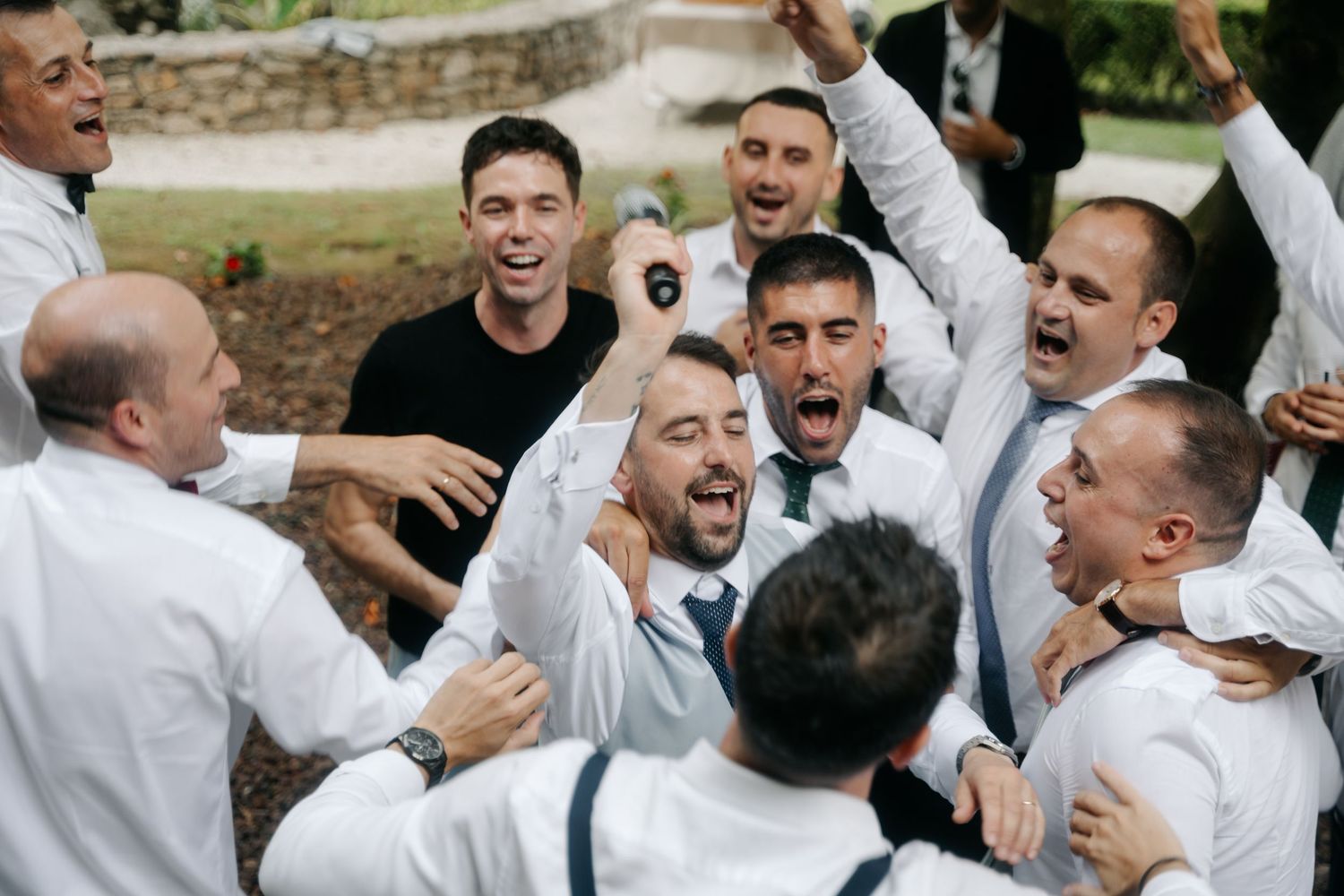 Groomsmen in white shirts celebrating and cheering together at an outdoor wedding event.
