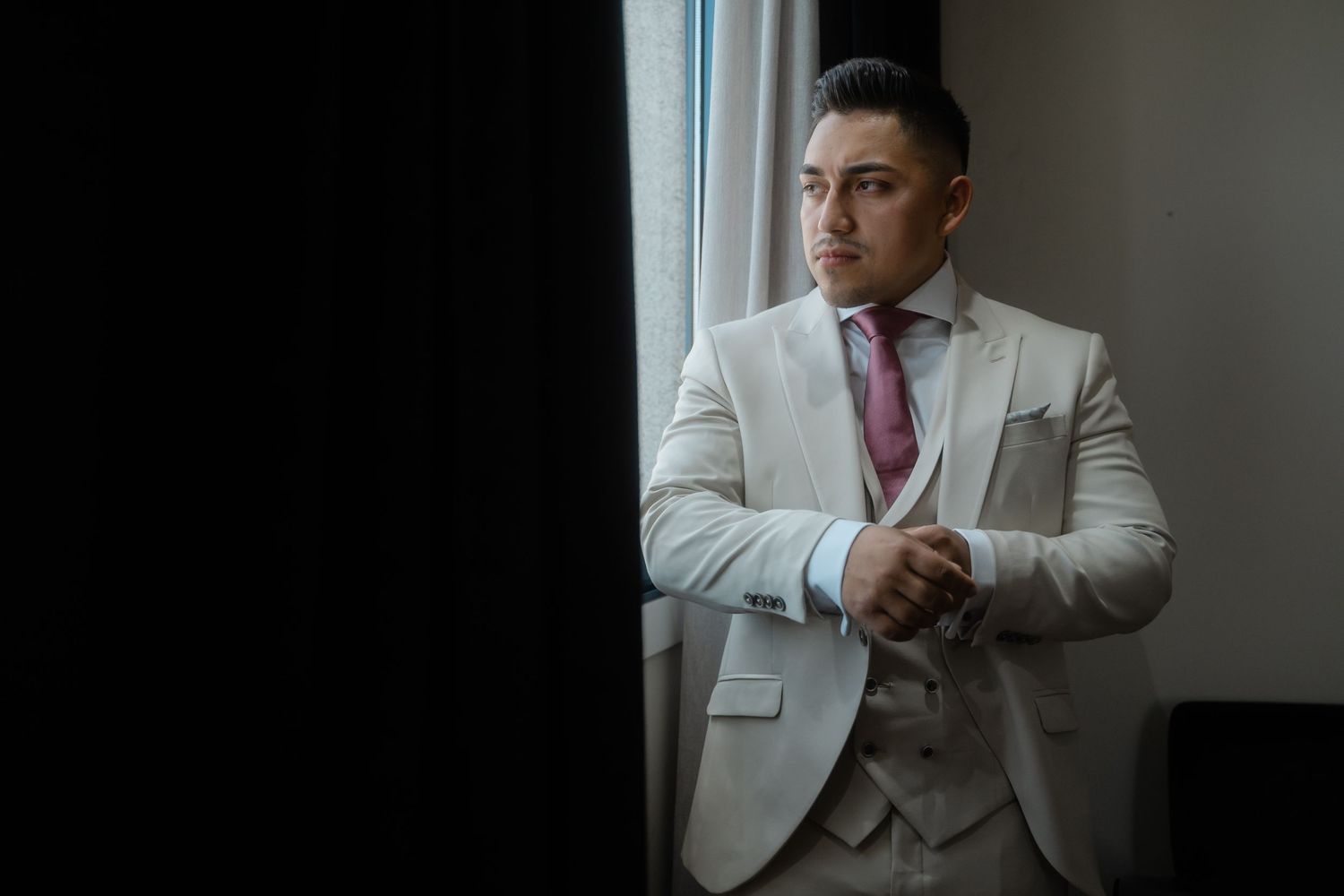 A person in a white suit jacket and pink tie poses in a professional photoshoot sequence.