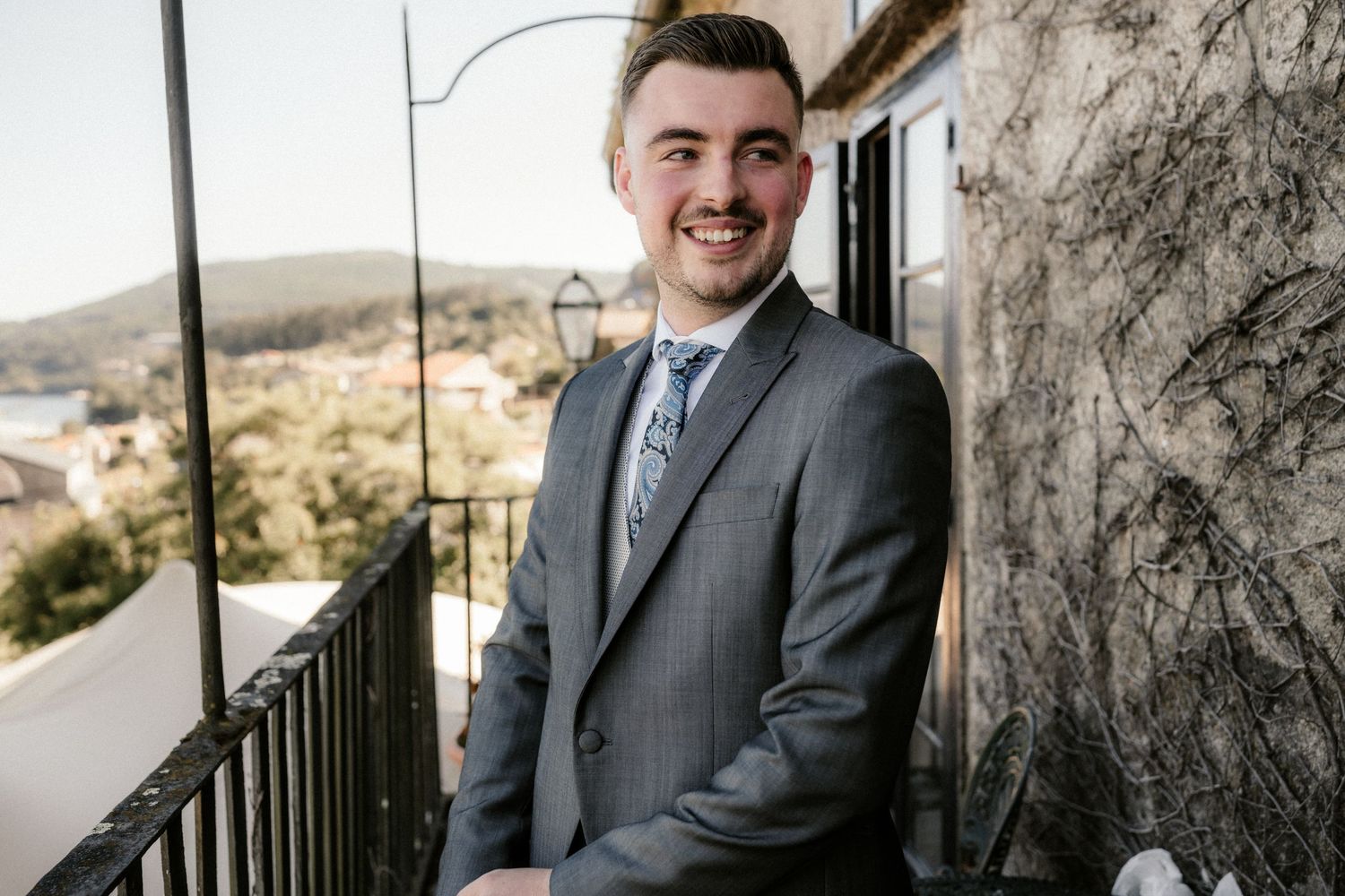 Professional wedding photography shows groomsmen getting ready in formal attire by a rustic stone wall.